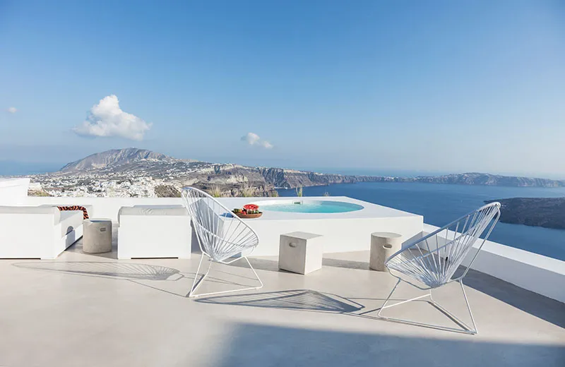 A minimalist lounge area with concrete seating and a swimming pool overlooking the ocean and mountains.