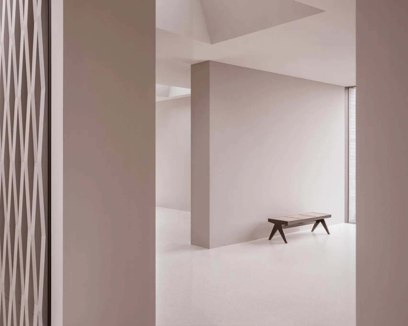 A minimalist white concrete space with a bench and a grid-like structure on the wall.