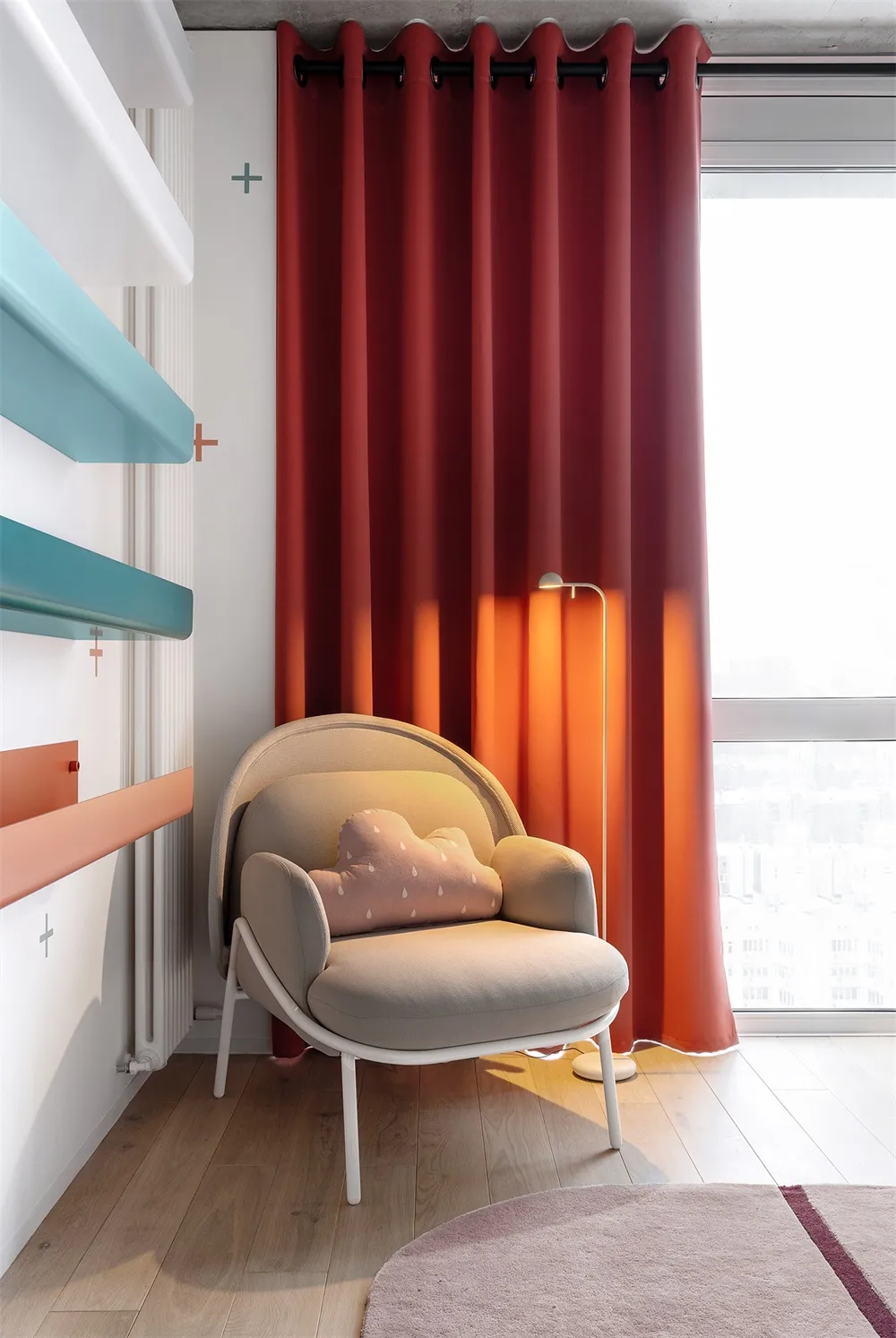 A modern living room featuring a fabric armchair with a pink cloud-shaped pillow, red curtains, and a wooden floor, under nat
