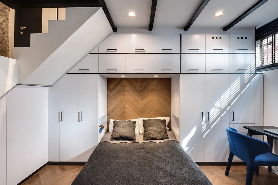 A modern minimalist bedroom with a bed, cabinets, and a window.