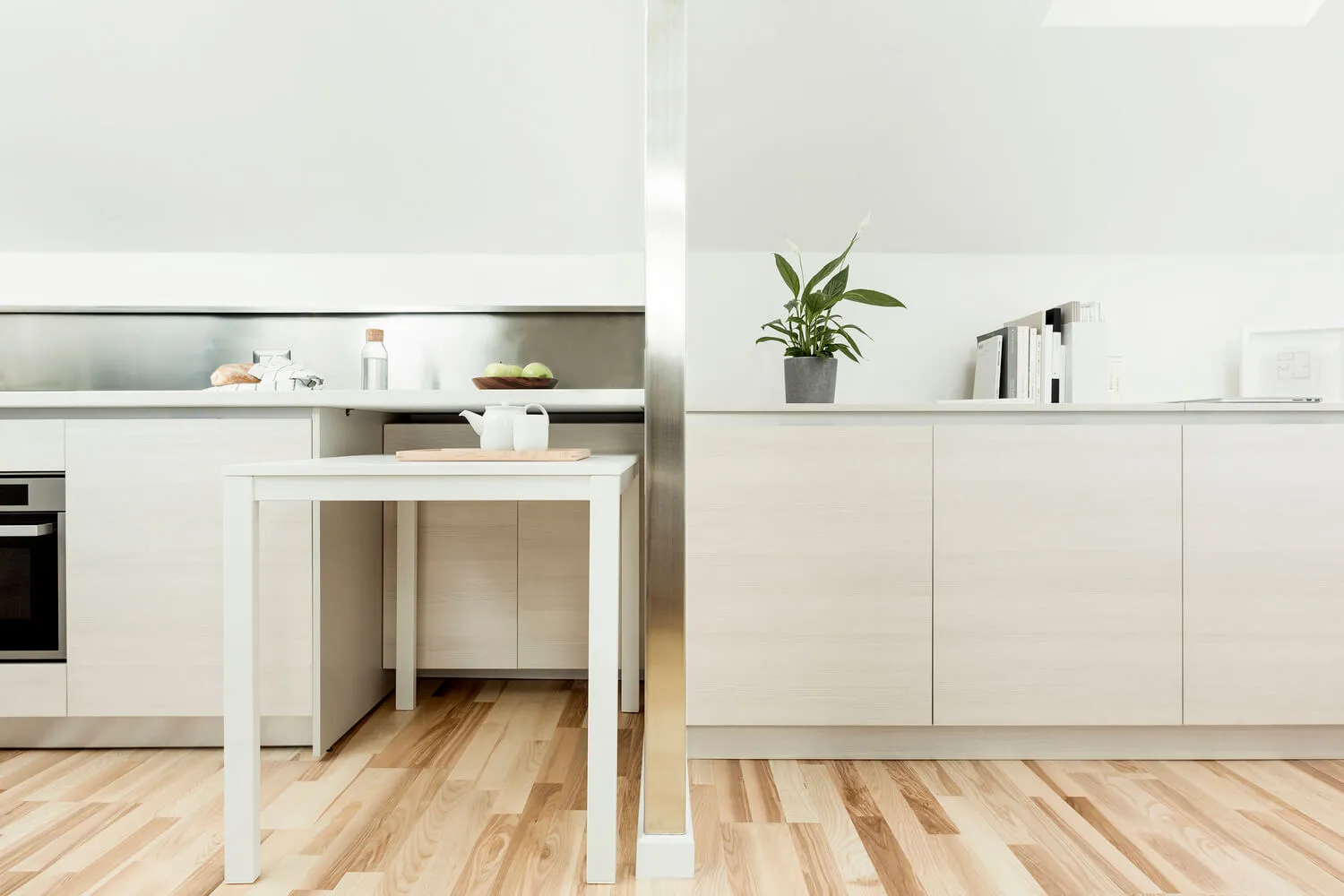 A modern minimalist kitchen with a white table and thinwood flooring.