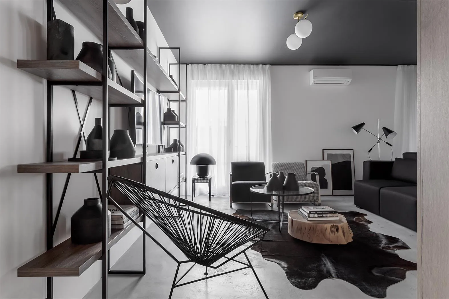 Modern minimalist living room with black, white, and wood furniture, concrete floor, and metal shelving.