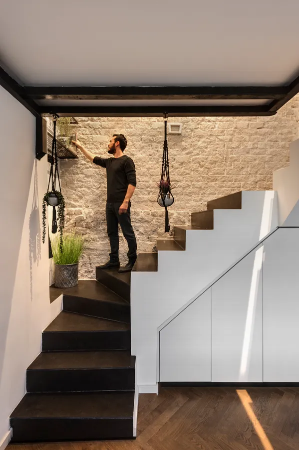 A man standing on a modern staircase made of concrete, with hanging plants.