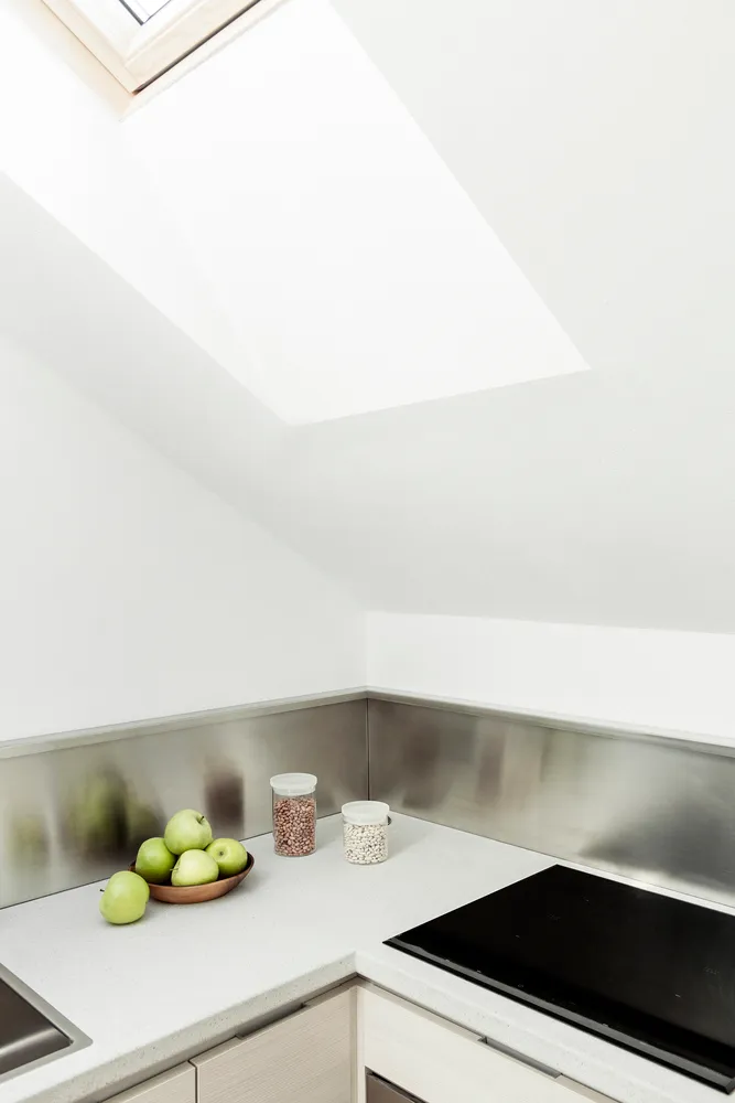 Modern kitchen counter with metallic backsplash and skylight above.