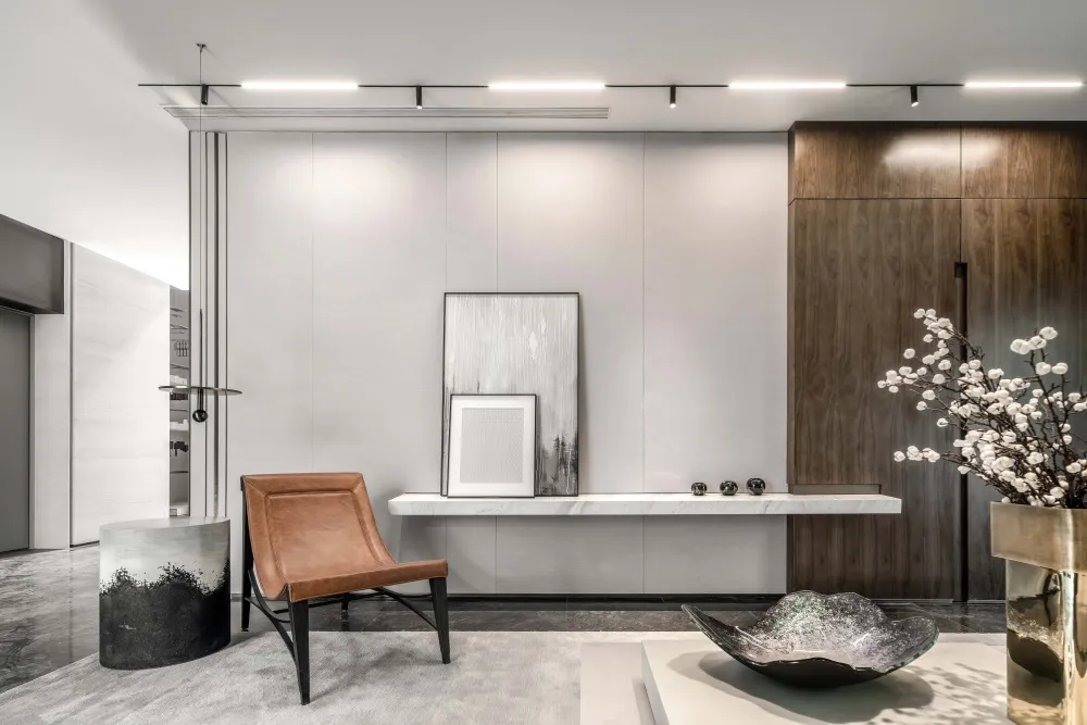 A modern living room with marble finishes, leather accent chair, and wooden cabinets.