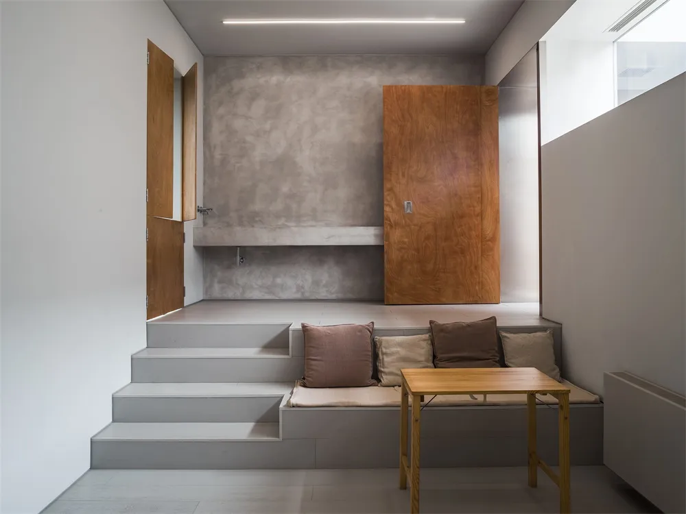 Modern living room with concrete walls, wood furniture, and steps.