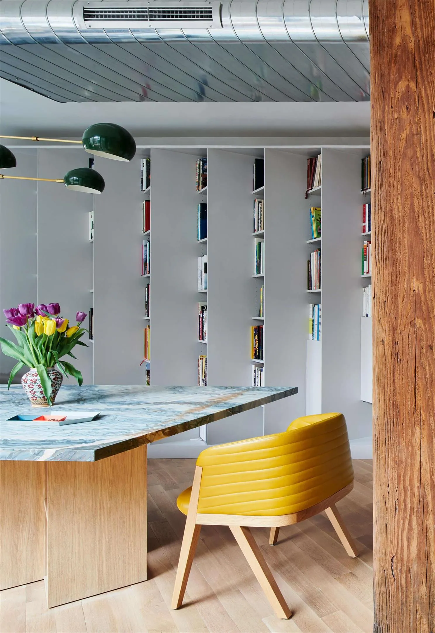 A modern study room featuring a marble desk with a yellow chair and a bookshelf filled with books.