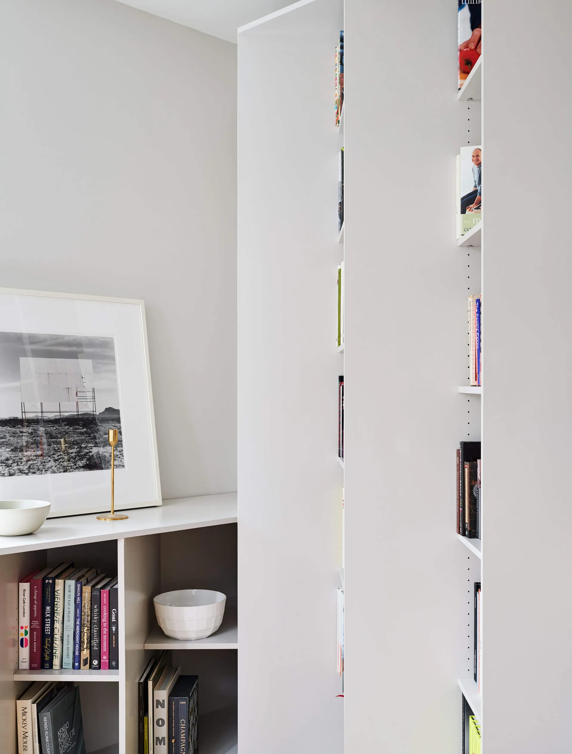 A modern home library with white shelves and a white framed artwork featuring a black and white photograph.