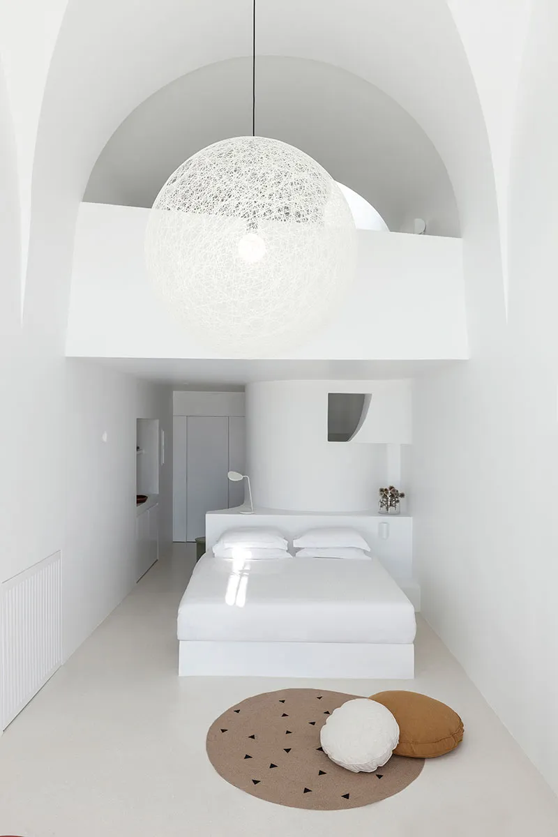 Minimalist bedroom with white bed, round light fixture, and fabric accents.