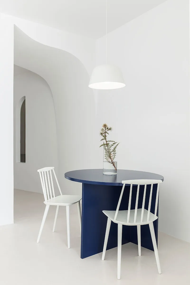 A modern minimalist dining room features a blue table with white chairs.