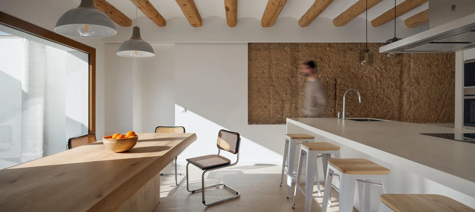 A modern kitchen featuring a wooden dining table with a bowl of oranges on it.