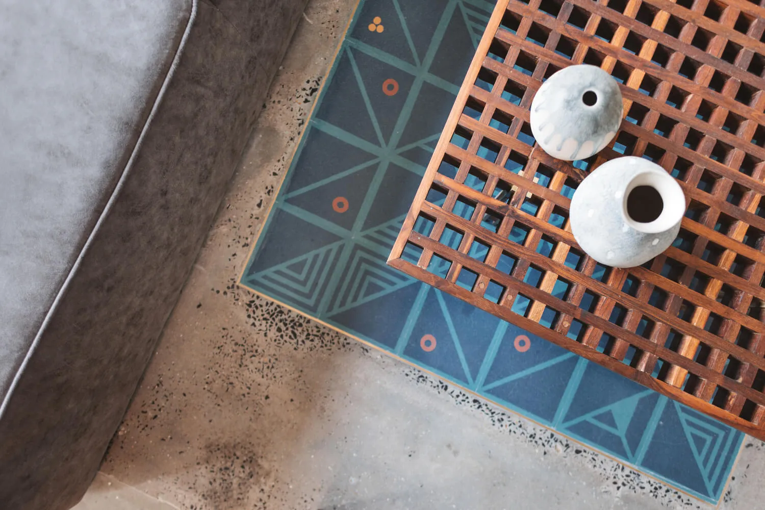 A wooden table with a geometric patterned tile background featuring concrete tiles and decorative vases.