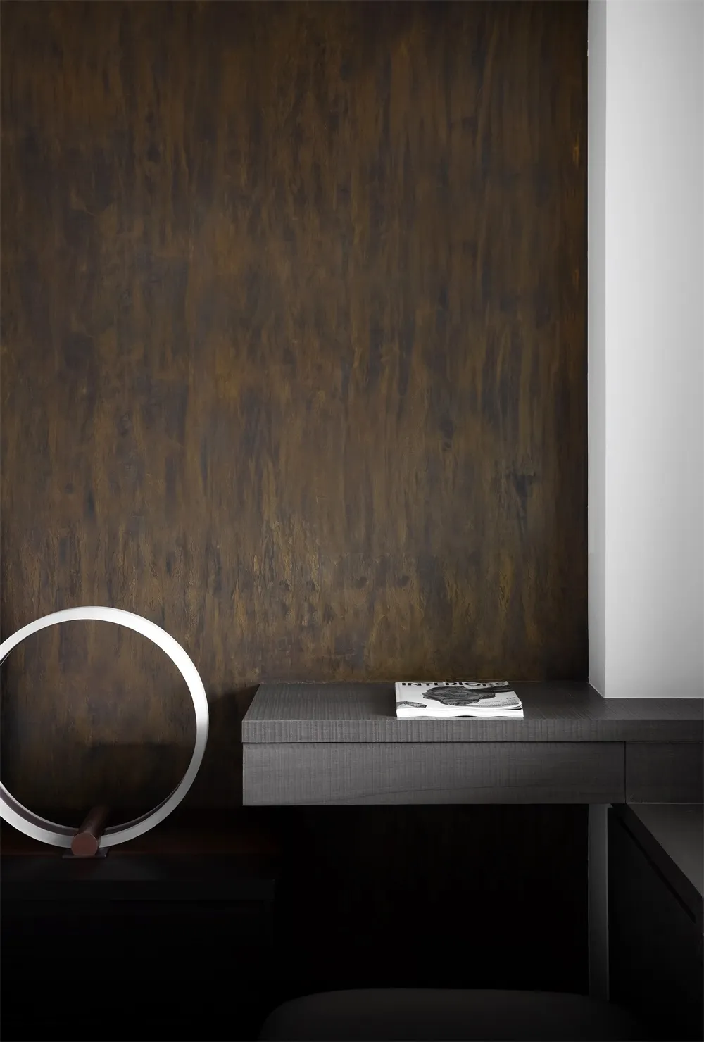A minimalist desk space featuring a black wooden floating desk with a metallic circular light fixture and a book.