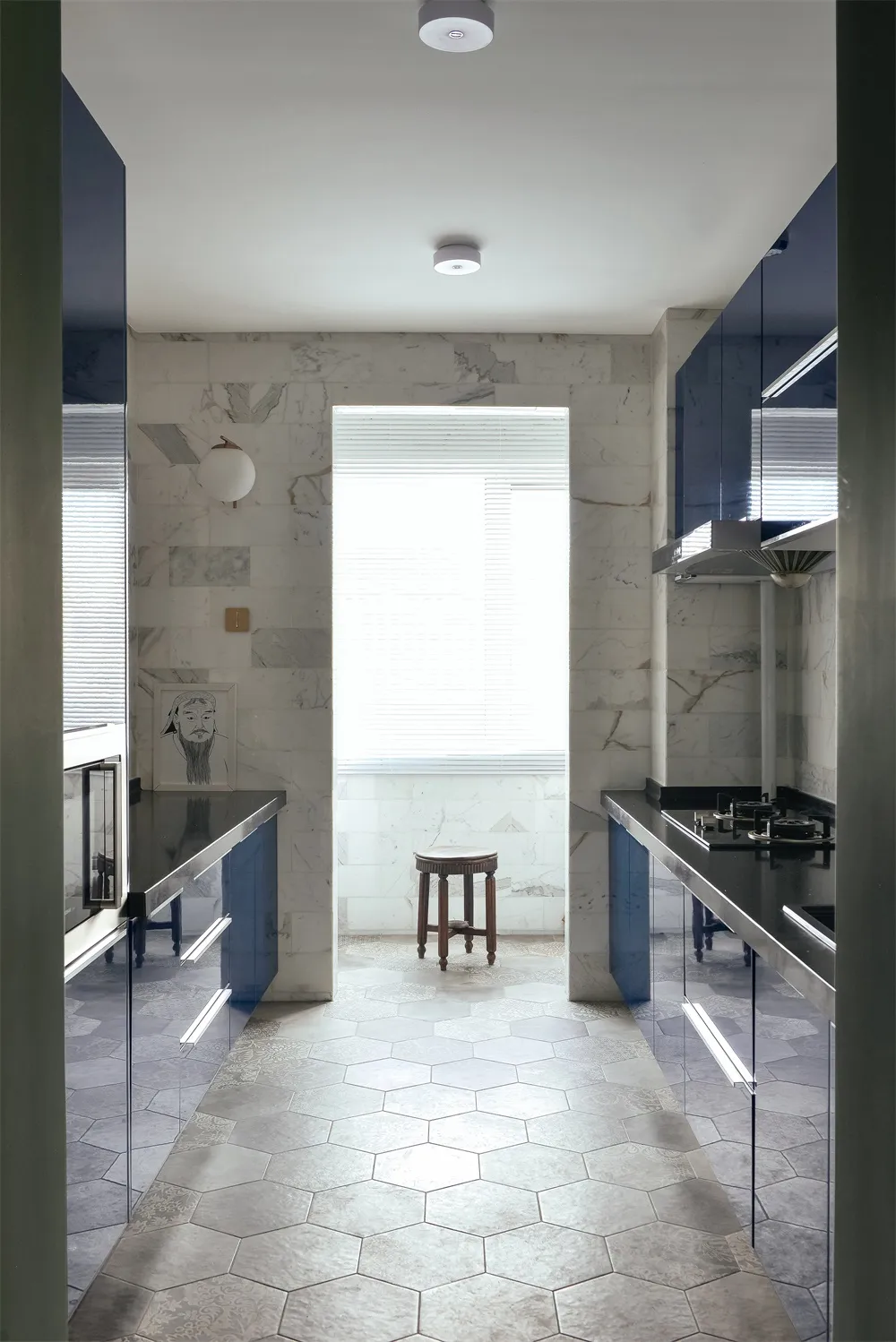 Modern minimalist residential kitchen with marble countertops and flooring, featuring a central window and stools.