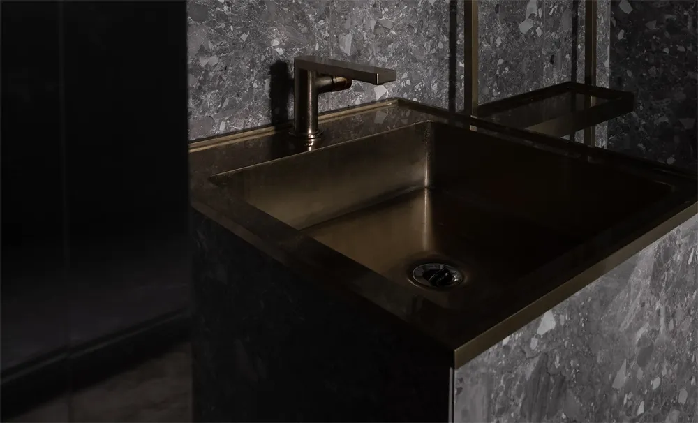 A modern bathroom featuring a brass sink and marble tiles.
