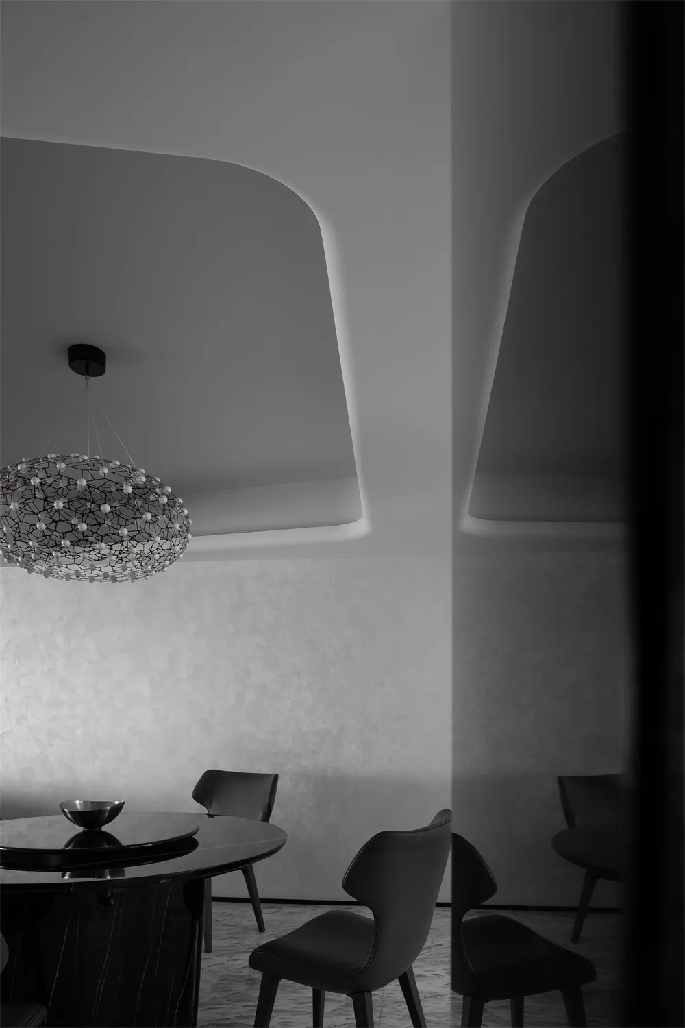 A modern dining room with black and white decor, featuring a round table, chairs, and a geometric chandelier.