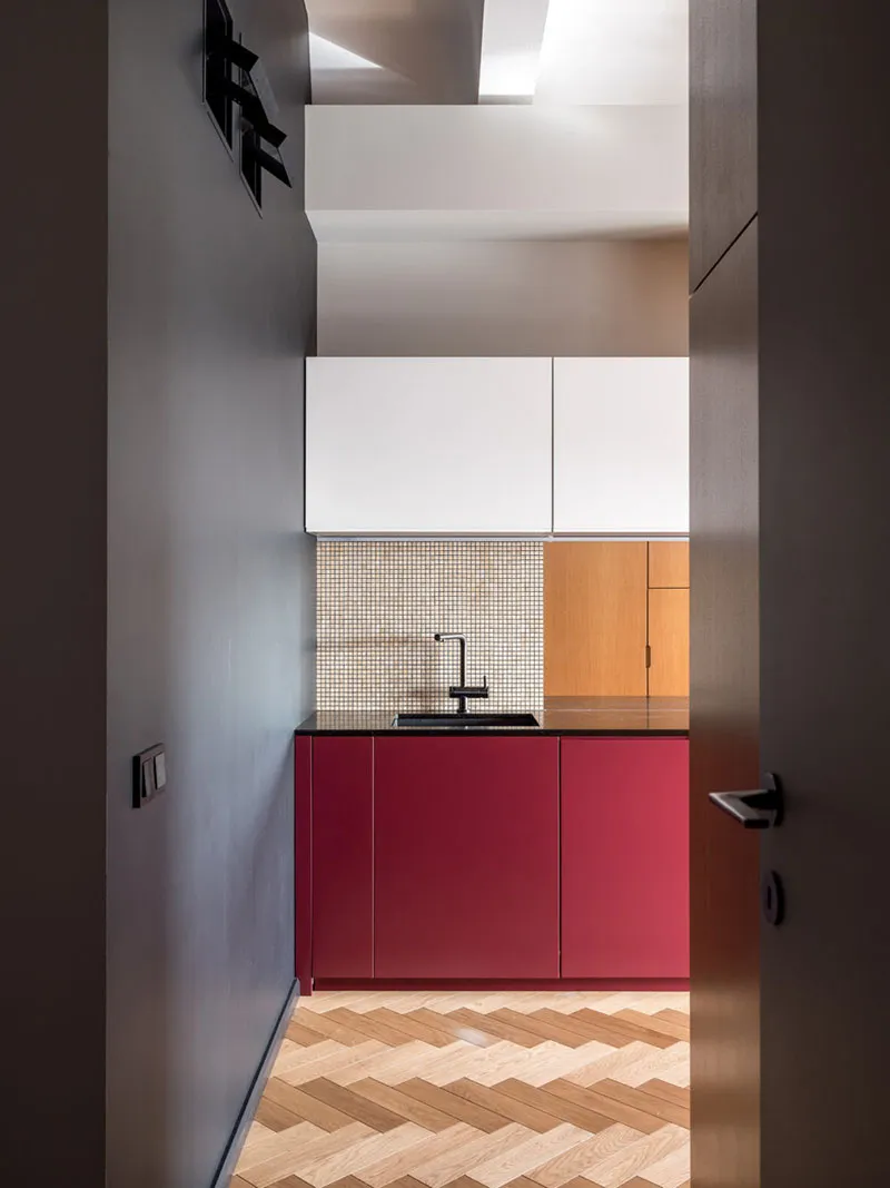 Modern kitchen featuring red cabinets, a wood floor with a herringbone pattern, and a white backsplash with small square tile