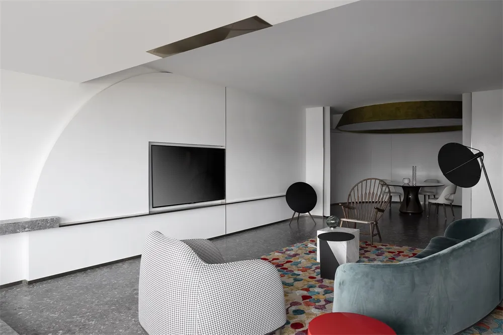 A modern living room with white walls, a black flat-screen TV, and a colorful rug.