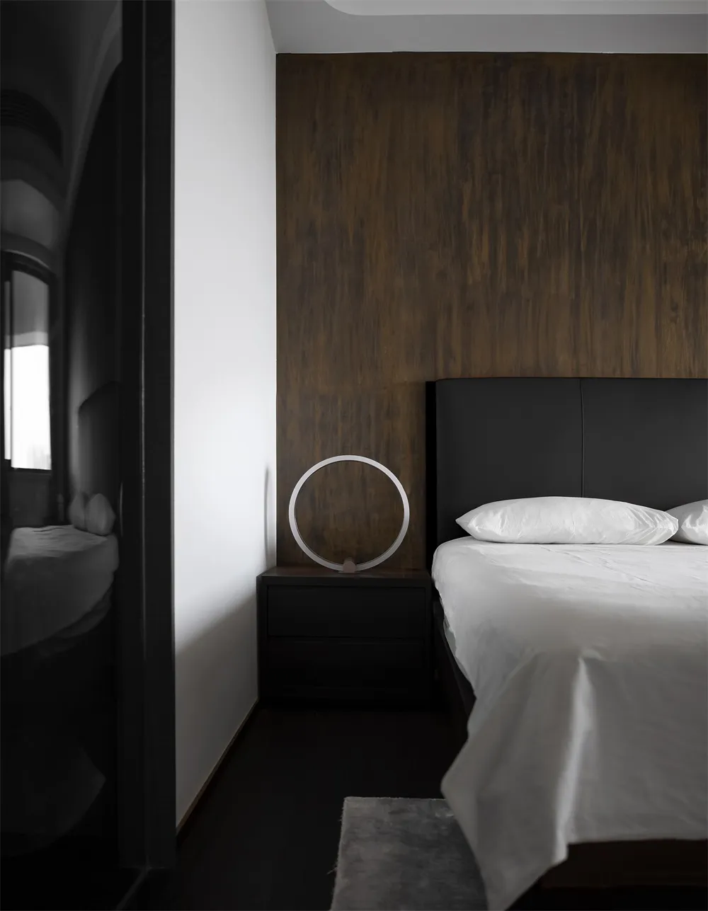 Modern minimalist bedroom featuring black leather headboard, wooden accent wall, and glass lamp on black nightstand.