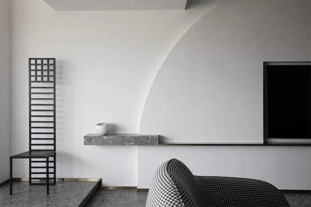A modern, minimalist living room featuring concrete walls and furnishings, with a black chair, a white bowl, and a black, pat