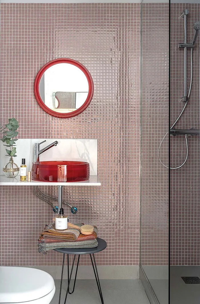 Modern bathroom featuring glass tiles on the walls and a red circular vessel sink.
