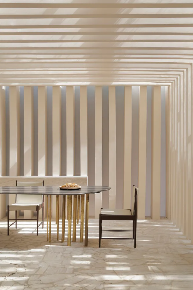 A modern minimalist dining room features stone accents and a metal dining table with minimalist white chairs.
