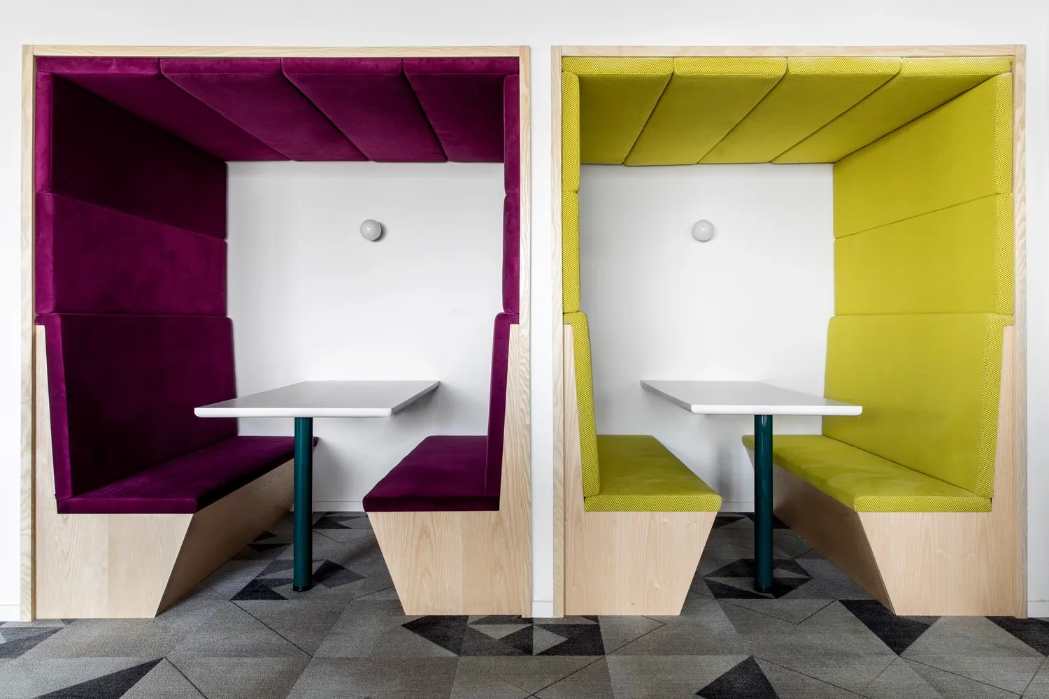 A photograph of two modern cafe booths with purple and yellow upholstered walls and white tables.
