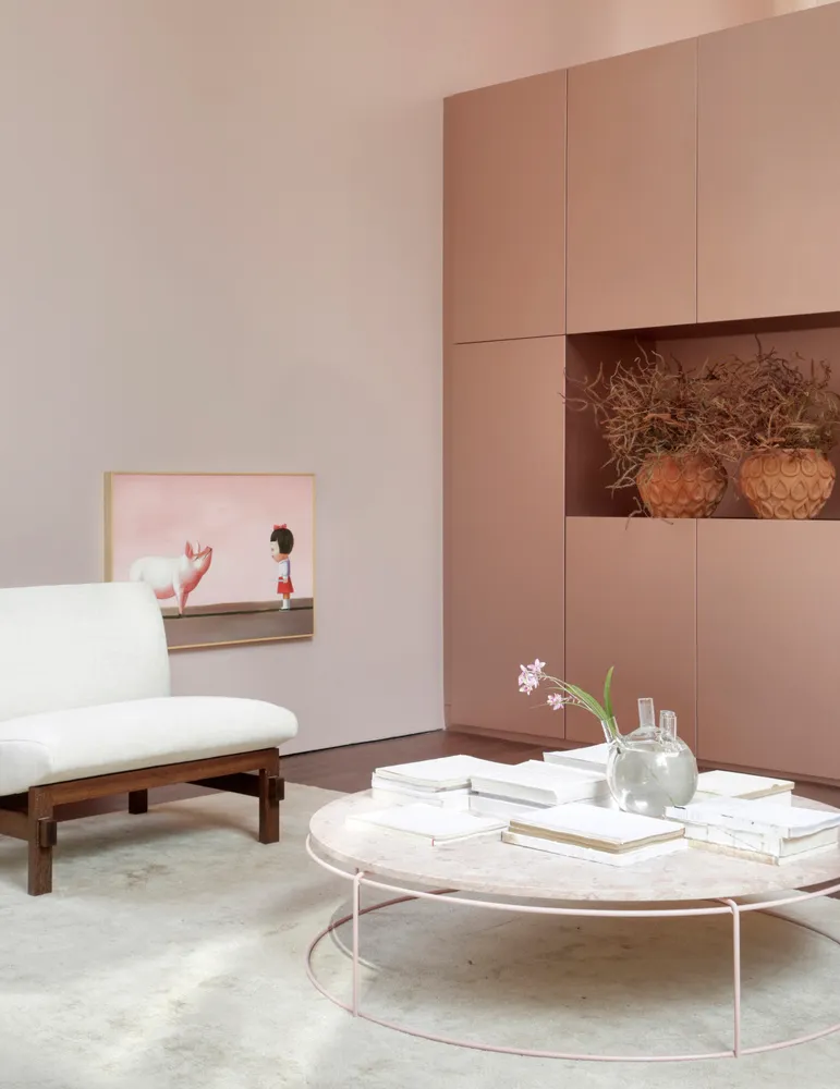 A minimalist living room with a concrete coffee table, white sofa, and pastel pink wall.