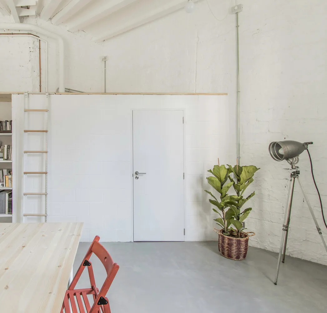 A minimalist living space with concrete walls, a white door, and a red chair.