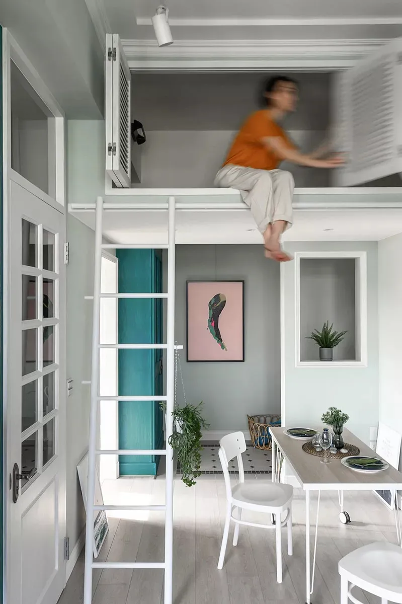 Minimalist design featuring a concrete loft with a white ladder, a dining table, and a person sitting on the loft.