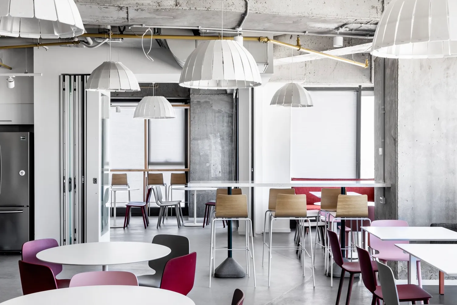 Modern canteen area featuring concrete walls, minimalist lighting, and colorful plastic chairs and tables.