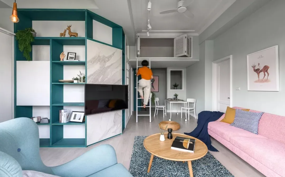 An image of a modern living room featuring a pink sofa, a blue armchair, and a green bookshelf.