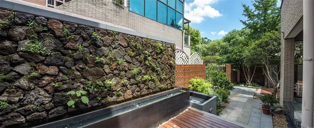 Modern landscape design featuring concrete walls, stone plants, and wooden deck.
