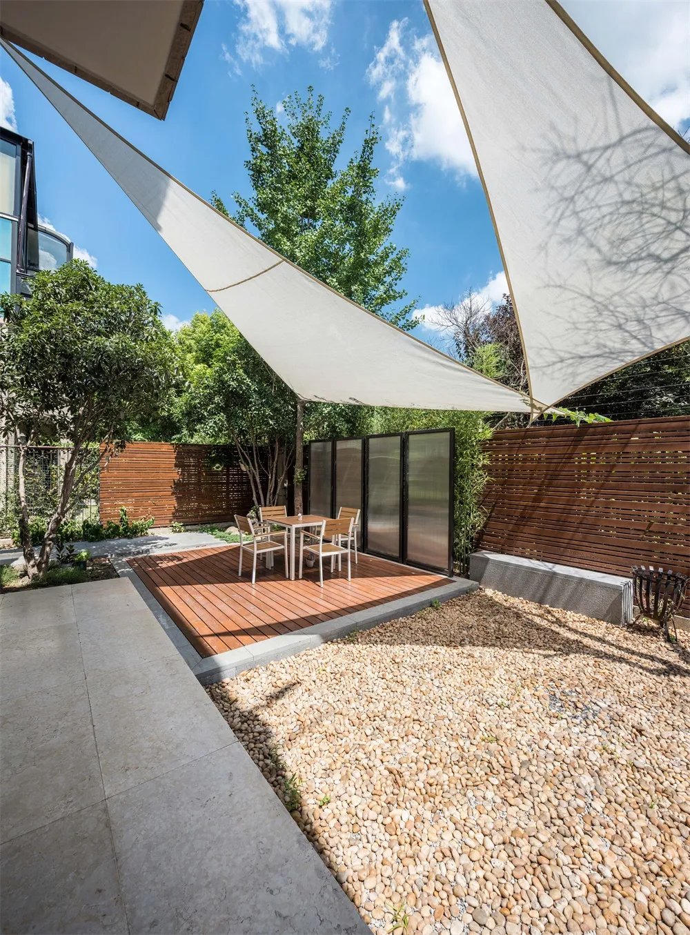 A modern outdoor space featuring a wooden deck, brown rocks, and a white canopy.
