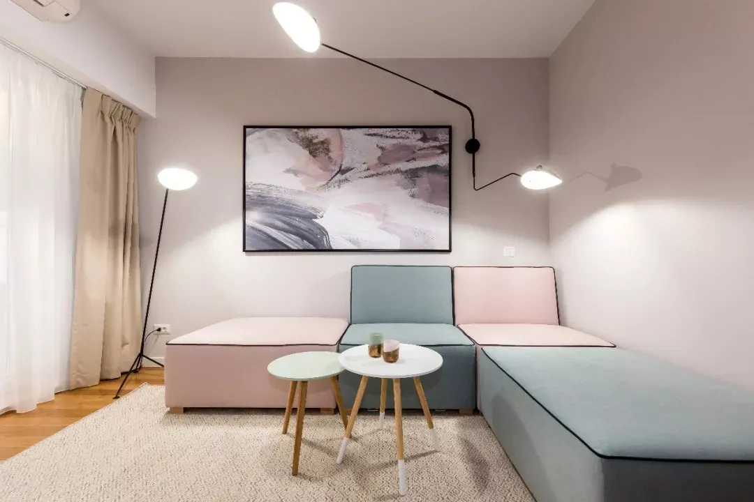 Modern living room with a couch composed of pink and blue cushions, a white and green table, and abstract artwork on the wall
