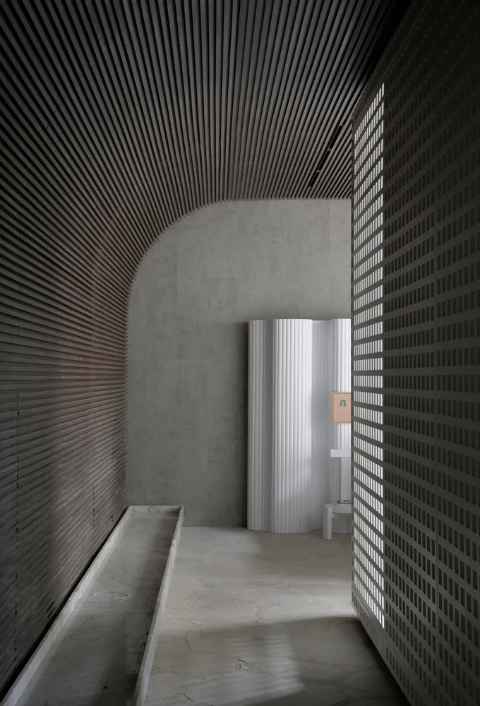 A minimalist concrete lobby interior with ribbed metallic panels and a textured marble floor.