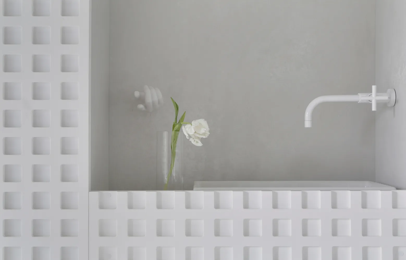 A minimalist modern bathroom with concrete walls, a white bathtub, and a white vase with a white flower on the edge of the tu