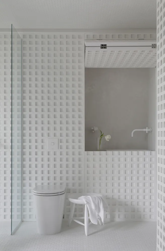 Modern minimalist bathroom with white porcelain tiles, white fixtures, and a vase of white tulips.