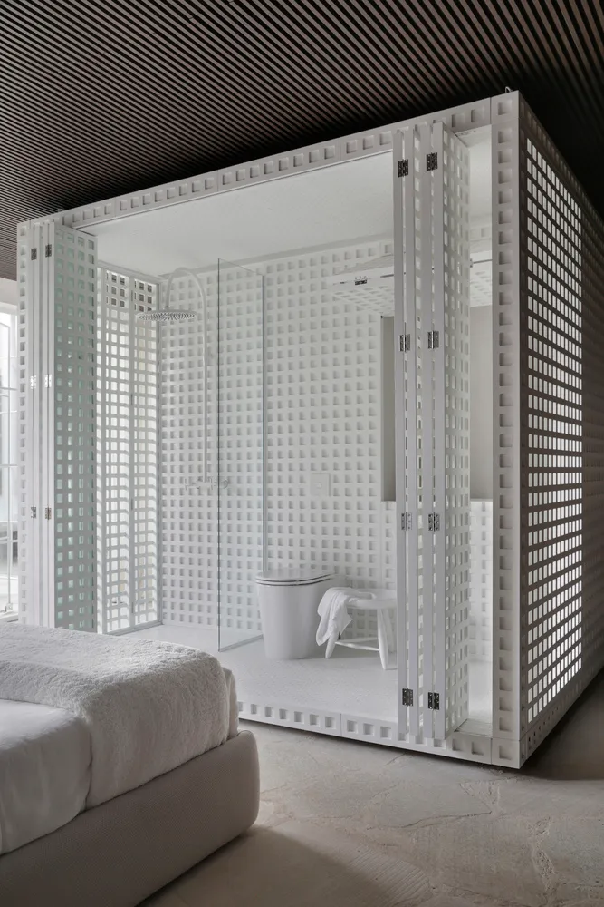 A modern bathroom with a white plaster shower enclosure and a white bed in the foreground.