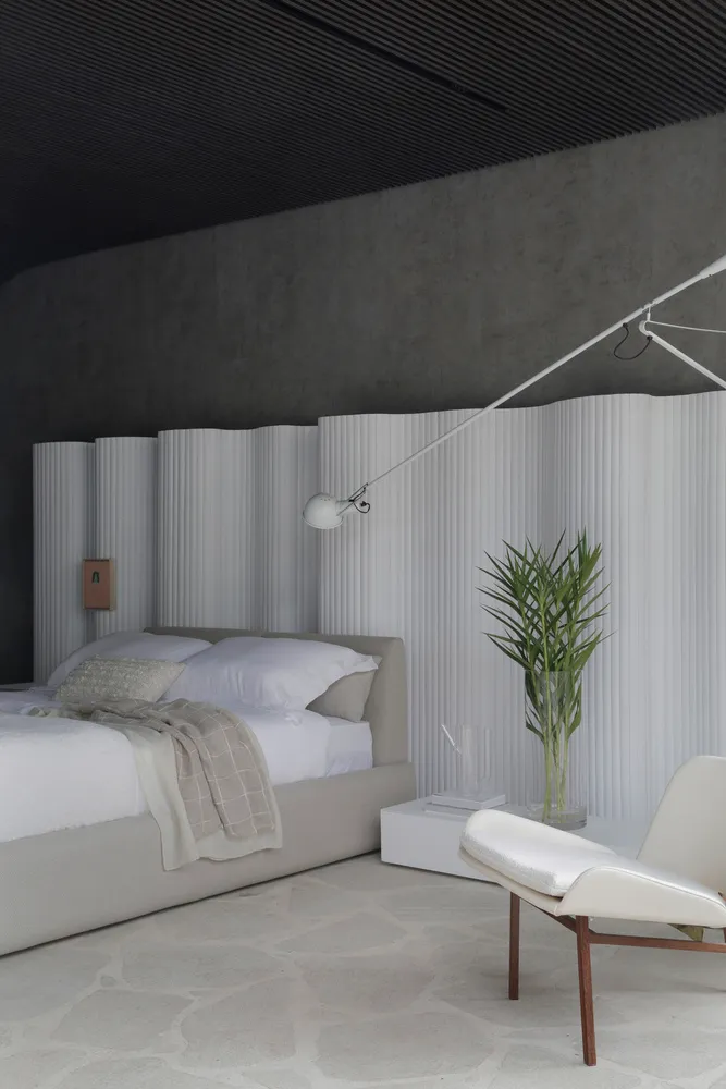 Modern minimalist bedroom with concrete walls, white furniture, and a single potted plant on a side table.