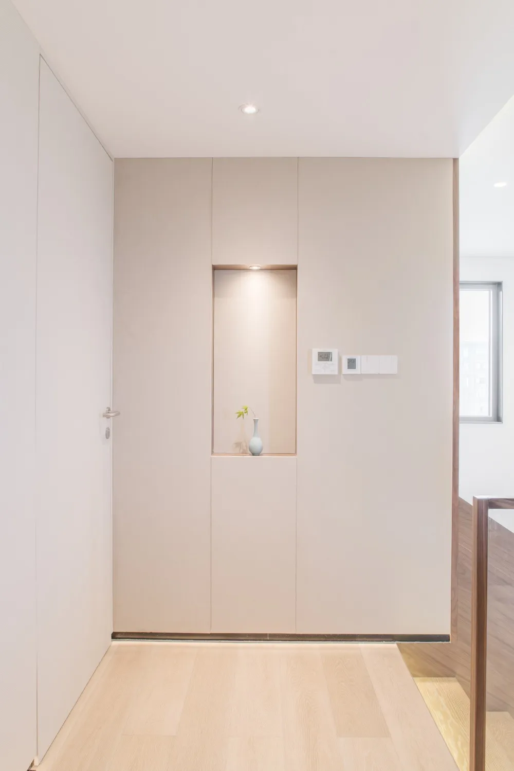 Minimalist interior design featuring light wood flooring and cream-colored panels with a small plant in a vase.