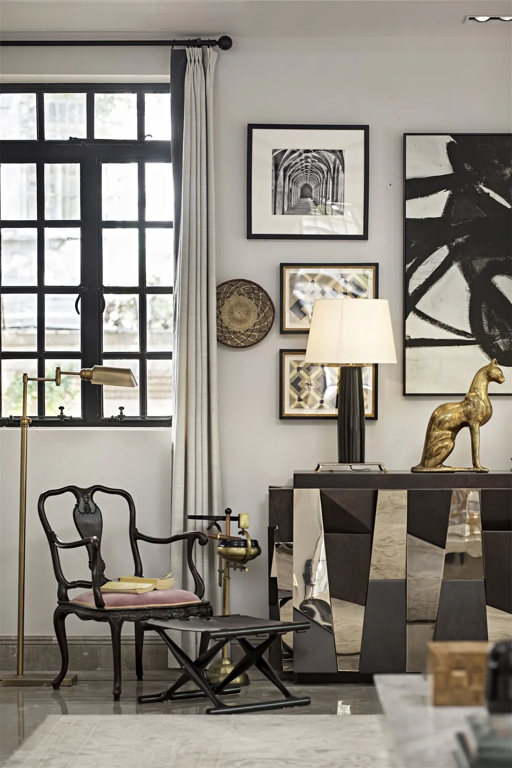 A modern living room featuring metallic accents, a cozy chair with a pink cushion, and framed artwork on the wall.