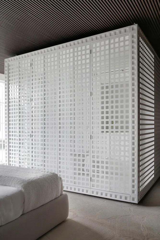 A minimalist bedroom with a white, textured plaster wall, featuring a bed with white bedding and a white, geometrically patte