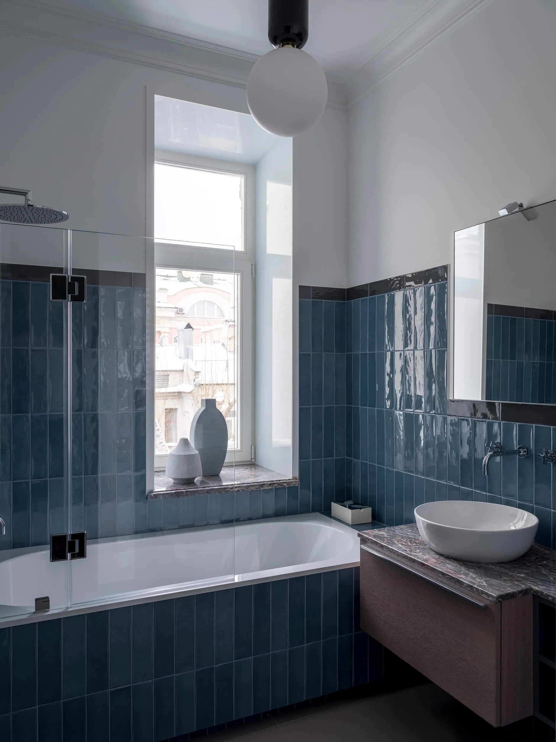 Modern bathroom with blue tiles, bathtub, sink, and window with natural light.