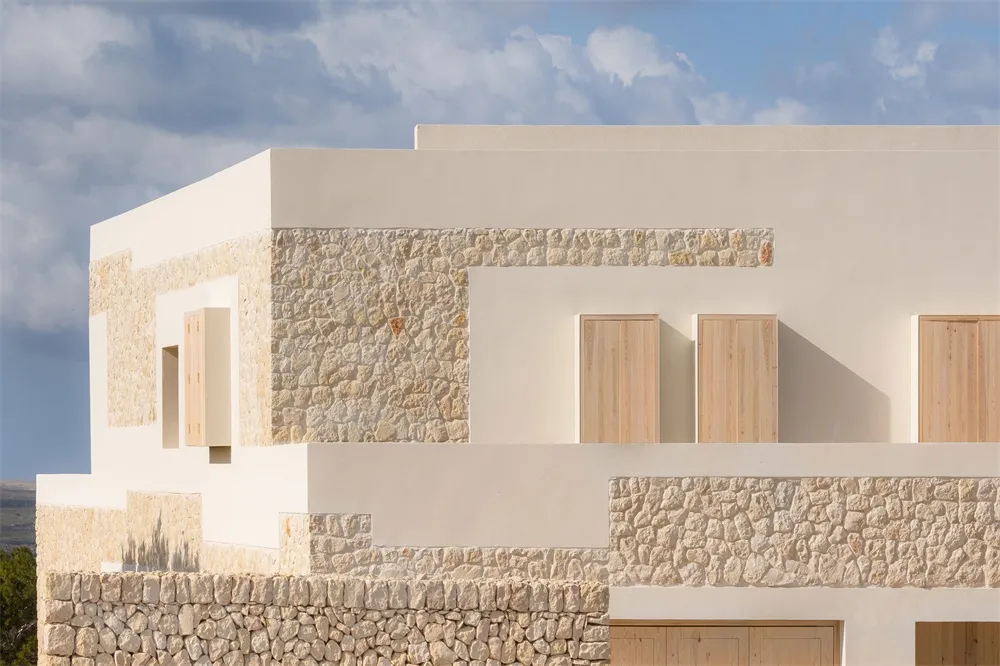 A modern building with concrete exterior walls and wooden accents against a blue sky with puffy clouds.