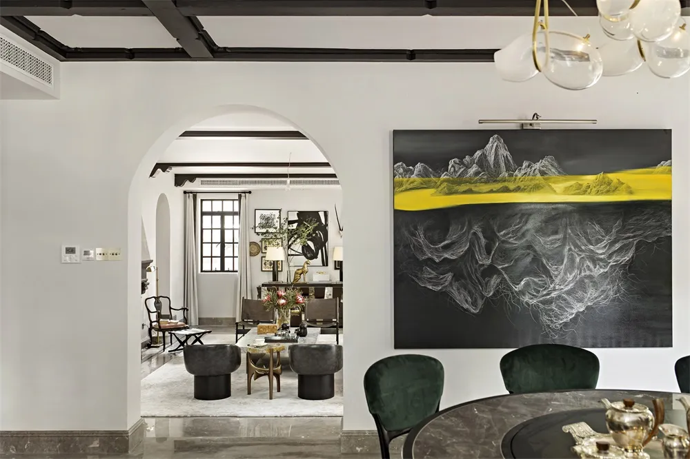 A modern dining room with a round marble table, green velvet chairs, and a large abstract art piece featuring yellow and blac