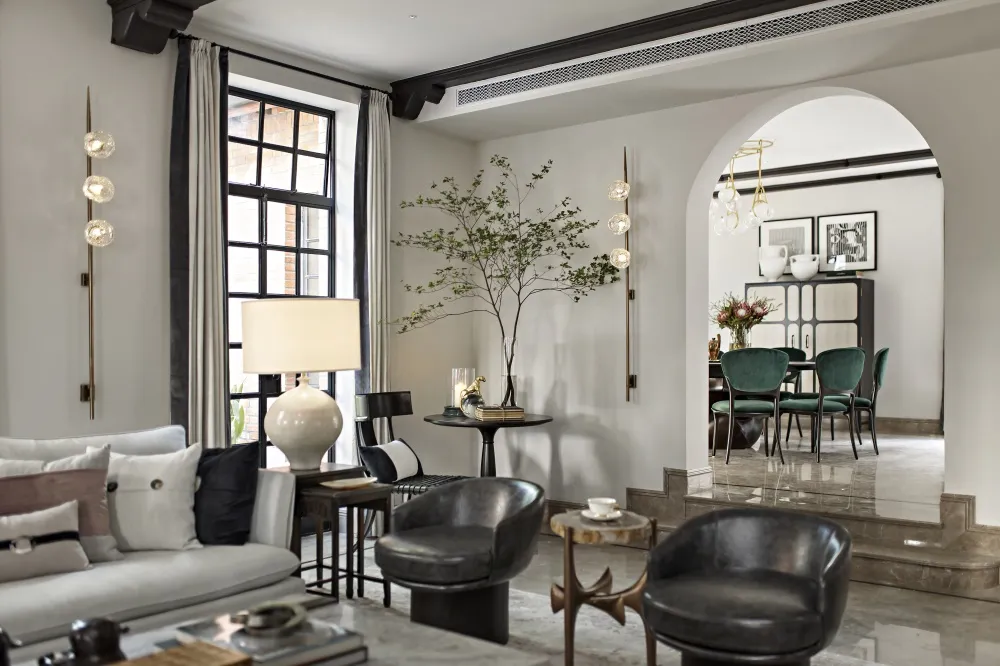 Modern living room with marble and glass decor, featuring a grey sofa, black chairs, and a glass table.