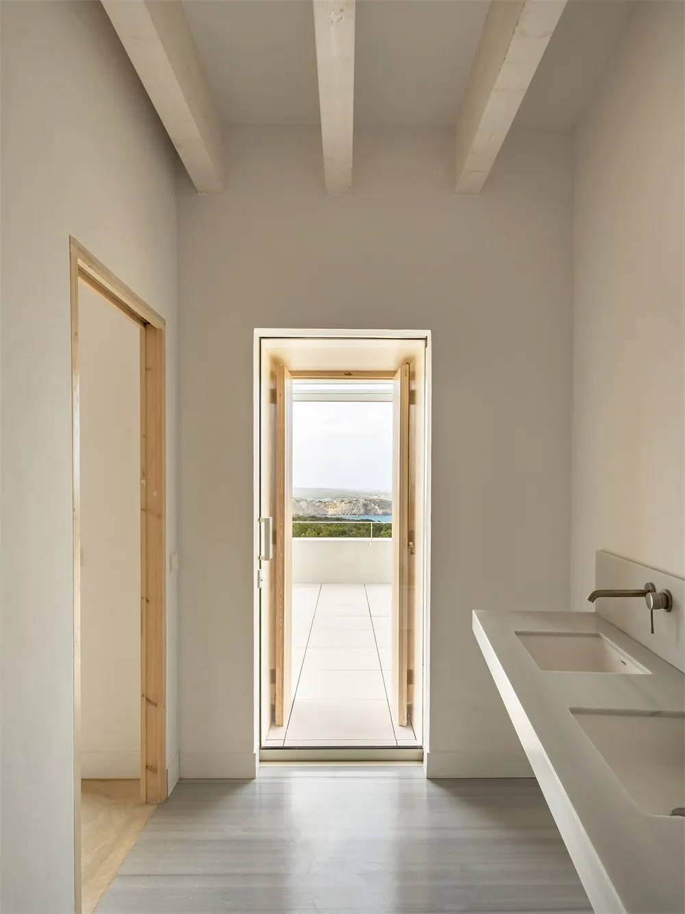 Modern minimalist bathroom with concrete floor and walls, glass door opening to outdoor patio.