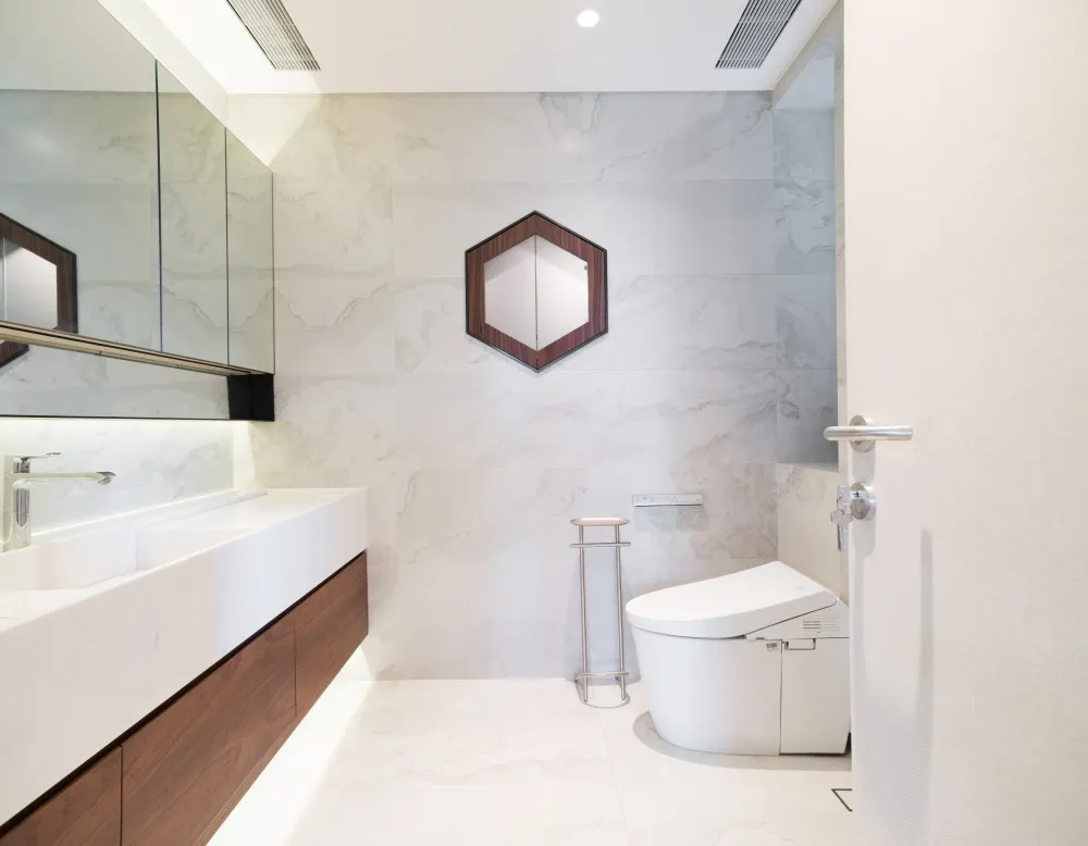 A modern bathroom featuring marble walls and floor tiles, a white toilet, and a wooden vanity with a single sink.