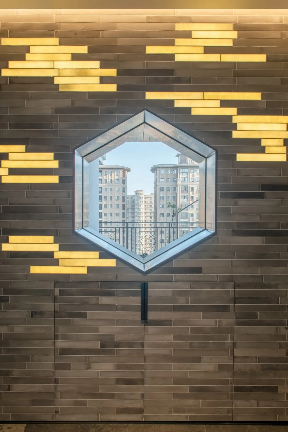 A modern concrete lobby with metallic accents and a hexagonal mirror reflecting nearby buildings and blue sky.